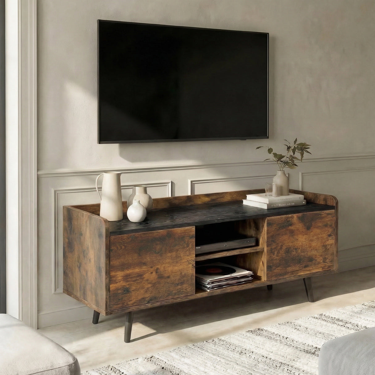 [Rustic | 112 cm] Larvik styled at an angle in a warm plastered room with wall-mounted TV, ceramic jug, vases, and books on dark top