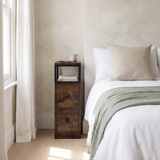 [Rustic] Narrow side table with storage beside a bed, holding a lamp and small bedroom essentials