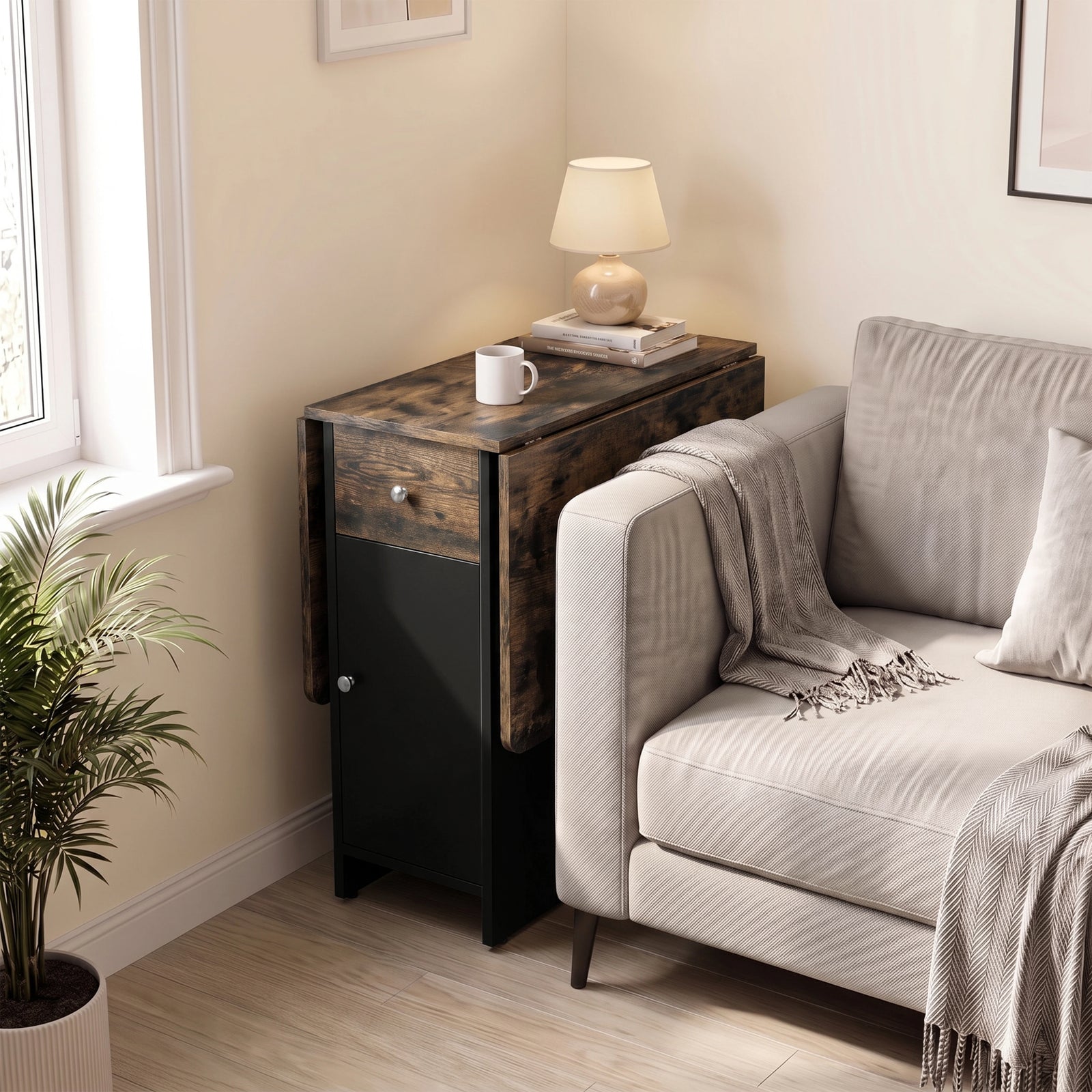 [Rustic] Small folding dining table closed beside a sofa featuring black cabinet with lamp, mug & books on wood-effect top.