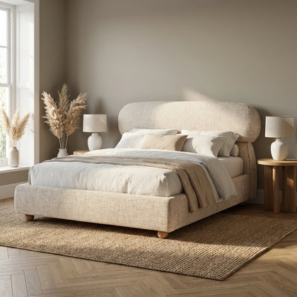 [Double | Beige] Upholstered bed frame showing curved headboard profile and low padded base on herringbone floor