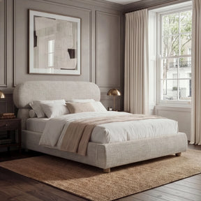 [King | Camel] Fabric bed with luxury rounded headboard beside nightstand with table lamp and natural daylight