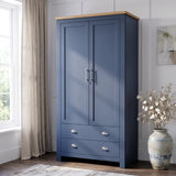 [Blue] two-door wardrobe with a light wood top and silver handles, set in a bright room next to a window with beige curtains and a decorative vase.