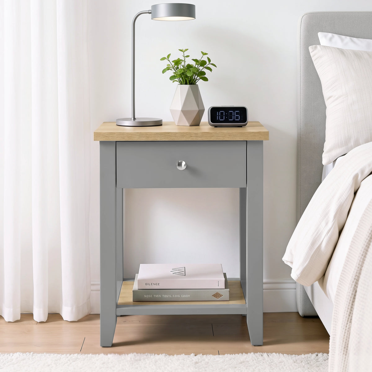 [Grey] Bedside lifestyle view with lamp, plant and clock on top, closed drawer and lower shelf