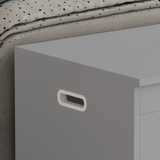 [Grey] Detail of grey shaker toy box flat lid surface and shaped side handle next to upholstered bed