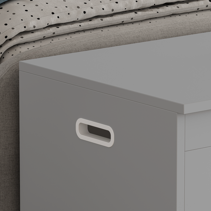 [Grey] Detail of grey shaker toy box flat lid surface and shaped side handle next to upholstered bed