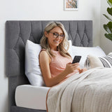 Woman relaxing on a single bed frame grey with a tufted linen headboard, using smartphone.