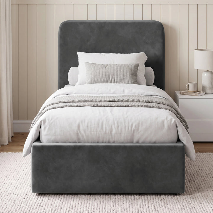 [Single | Grey] Angled room view with rounded headboard, white bedding, desk, bedside table, curtains, and rug