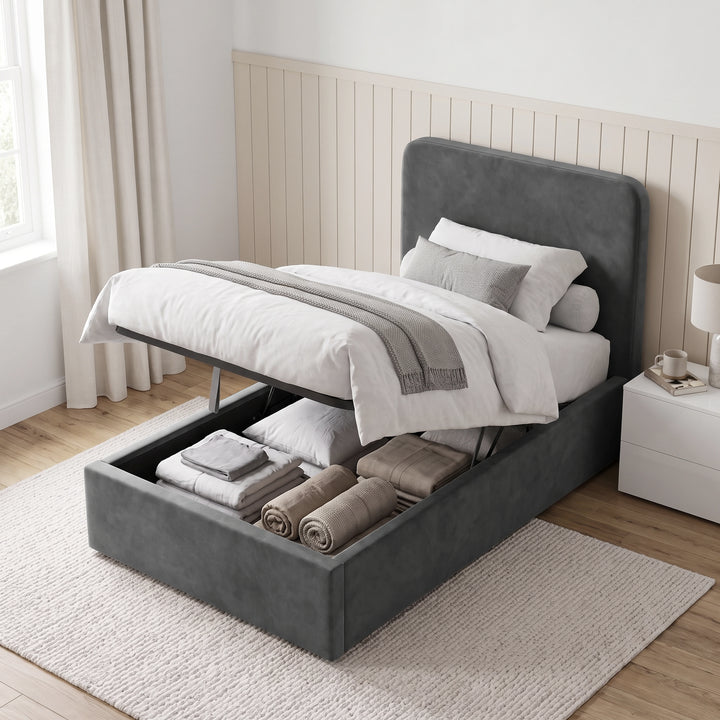 [Single | Grey] Side-lift storage view with raised mattress base, folded bedding, rugs, pillows, and bedside table