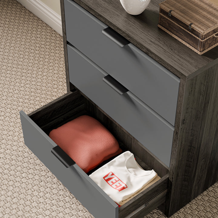 [Wooden Grey+Grey] Skova chest of drawers viewed at angle, bottom drawer pulled out on patterned carpet