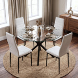 [Glass] Round glass dining table featuring sturdy black crossed legs, styled with four dining chairs, tableware and a vase.