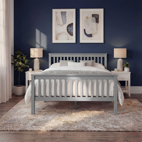 Grey wooden double bed frame with vertical slatted rails, with layered bedding, and placed in a natural light bedroom