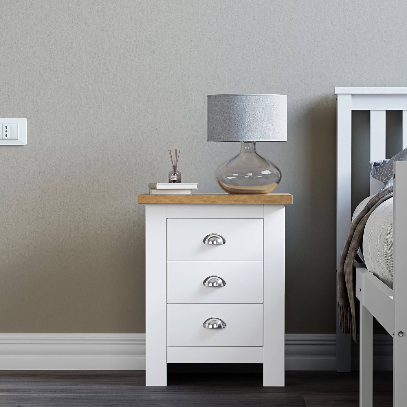 Small white bedside table with handles, featuring a cozy top surface with a lamp and books.