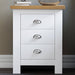 Small white bedside table with handles, featuring a cozy top surface with a lamp and books.