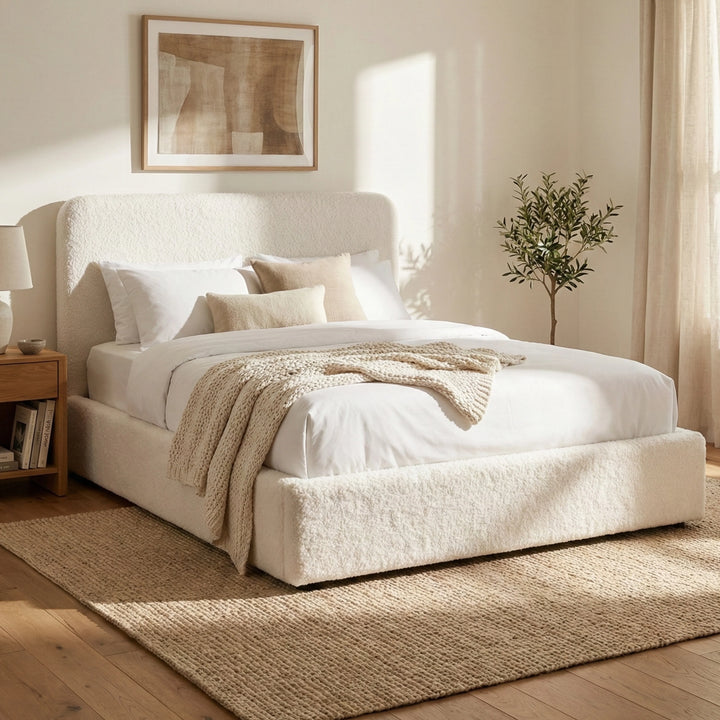 [White | King] King Sofna boucle ottoman bed three-quarter, rounded headboard beside oak nightstand in sunlit room