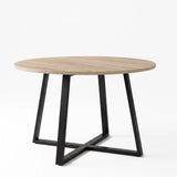 [Sonoma Oak] Round light oak-effect dining table in a studio view with the tabletop on a black iron cross base.