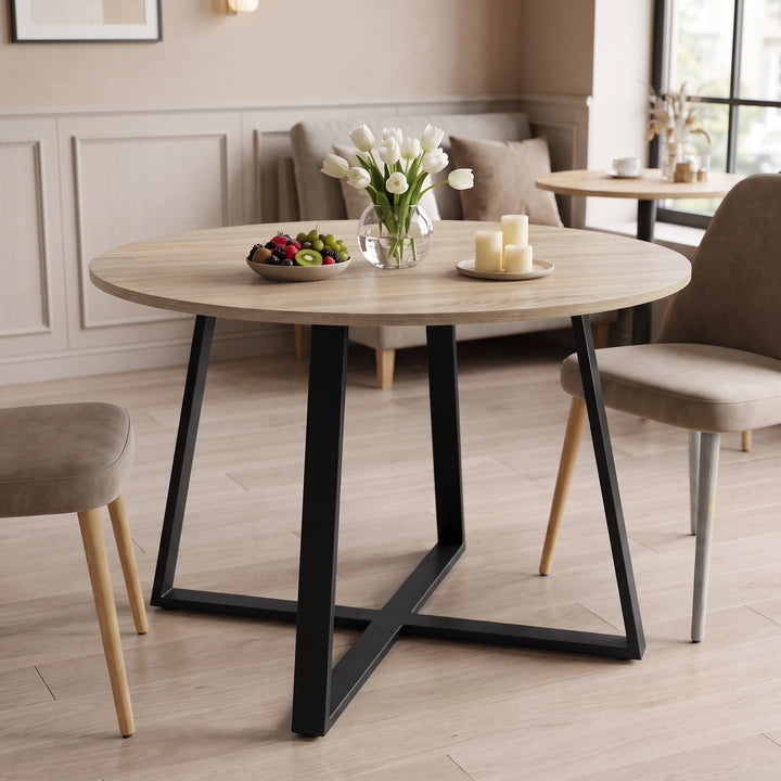 [Sonoma Oak] Round light oak-effect dining table in a bright room with flowers, fruit and candles on the tabletop.