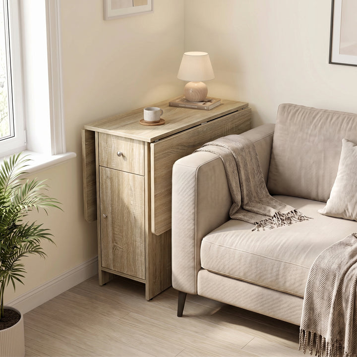 [Sonoma Oak] Small folding dining table fully closed beside a sofa and window, with a lamp, books and mug on its narrow top.