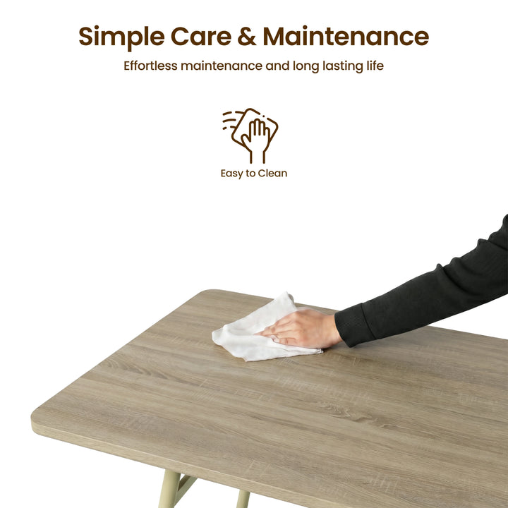 [Sonoma Oak] Torvi dining table easy-clean surface detail showing person wiping the oak-effect MDF tabletop with a cloth on a white background