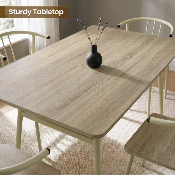 [Sonoma Oak] Torvi dining table and chairs overhead close-up showing oak-effect tabletop surface with a small vase and four cream metal arm chairs around it