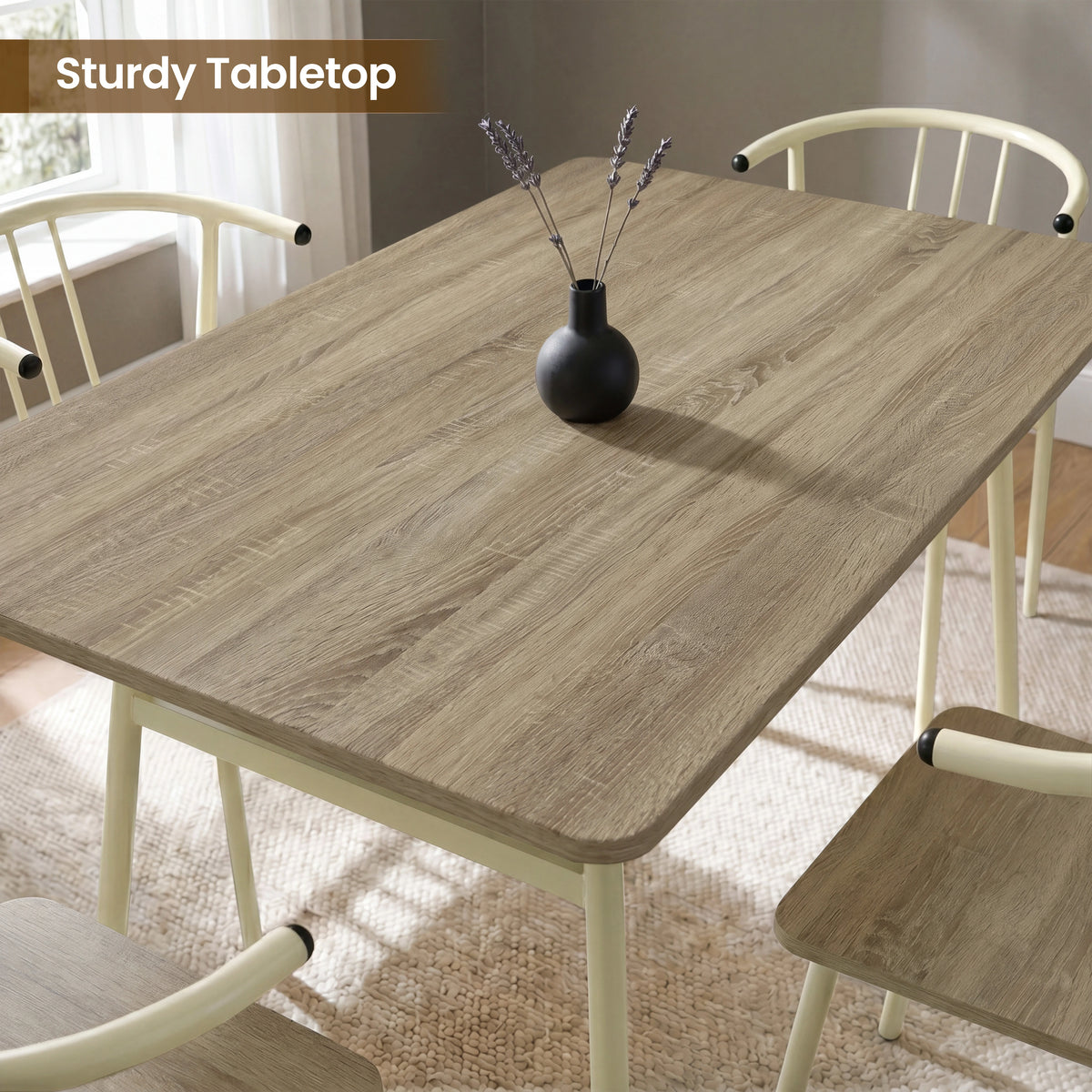 [Sonoma Oak] Torvi tabletop close-up showing wood grain, rounded corners, a black vase, and cream chair backs.