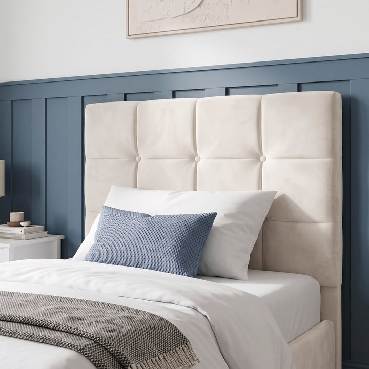 [Single | Beige] upholstered headboard in a warm belge velvet fabric, shown on a bed in a styled bedroom with blue paneled wall, white bedding, and a blue accent pillow.