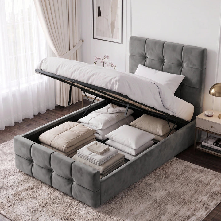 [Single | Dark Grey] tufted velvet storage bed with the mattress lifted open to show bedding and folded linens inside, styled in a bright modern bedroom with a nightstand, lamp, curtains, and framed wall art.