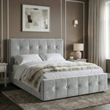 [Double | Grey] Side angle of tufted ottoman bed against taupe wall with white panel moulding and brass wall sconce glowing