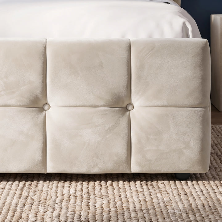 [King | Beige] A close-up of a cream-colored upholstered bed frame with a tufted panel design and decorative buttons, resting on a woven jute rug.