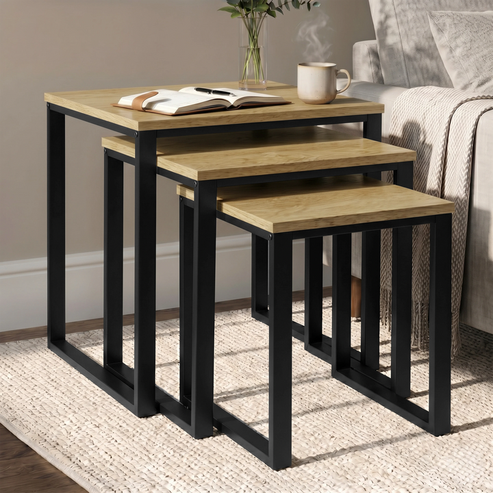 [Oak] Stackora set of 3 nesting tables angled view in a living room with sofa and accessories on oak tops