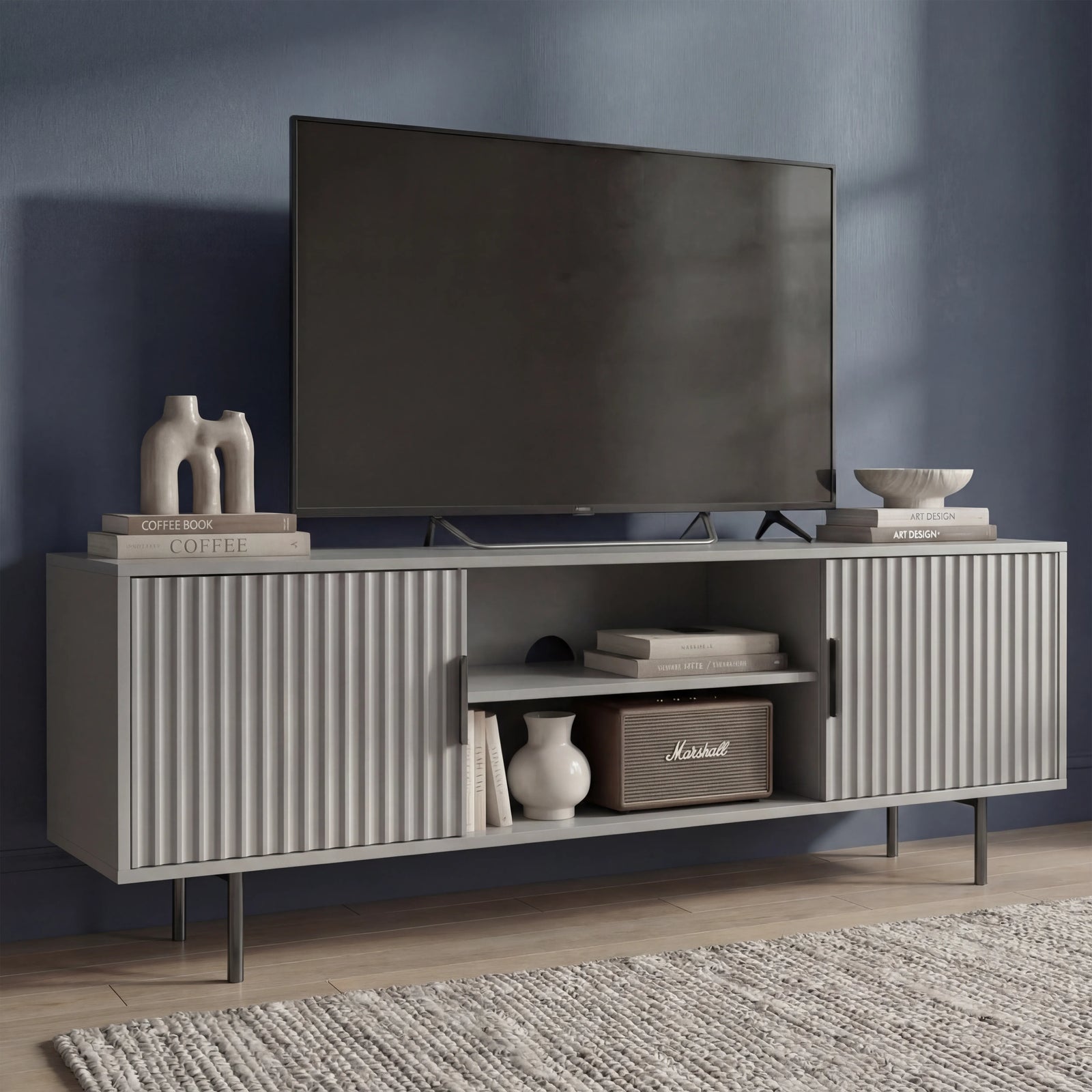 [Grey] Flutrina 140cm TV unit on textured rug, vertical fluted side doors flank centre shelf with vase and Marshall speaker