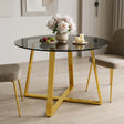 [Tinted] round dining table with a tinted glass top and a polished gold metal base, styled in a modern dining room with two beige upholstered chairs, a vase of flowers, and candles.