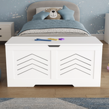 White toy storage bench in a child's bedroom with a bed and teddy bear in the background.