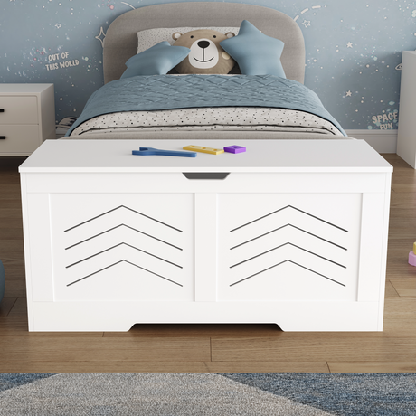 White toy storage bench in a child's bedroom with a bed and teddy bear in the background.