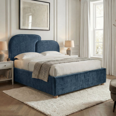 Double bed upholstered in blue fabric placed near a window with light bedding and neutral bedroom decor