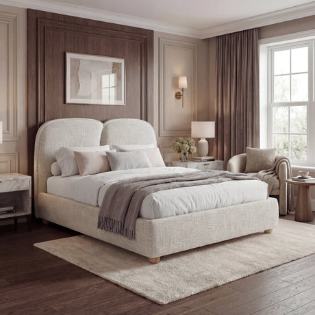 King-size bed frame placed near tall windows, with softly beige upholstered fabric and matching bedding layers