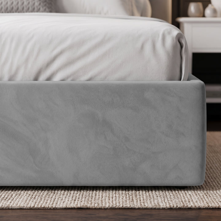 [Light Grey | King] close-up of a bed frame upholstered in textured grey velvet, shown with white bedding and a woven beige rug in a softly lit bedroom setting.