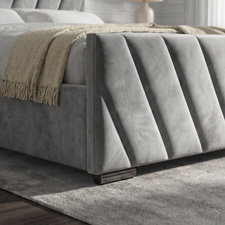 Close-up view of the footboard of a grey velvet ottoman bed, highlighting its smooth fabric and shape