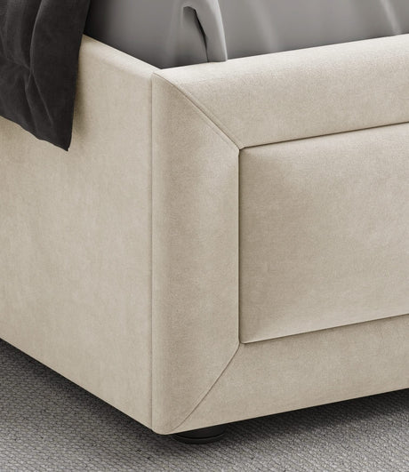 [King | Beige] Close-up of footboard corner showing raised rectangular panel and angled velvet edge on grey carpet