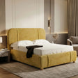 [Double | Yellow] Side angle of mustard fabric bed with curved wingback headboard, marble nightstand and brass sconce