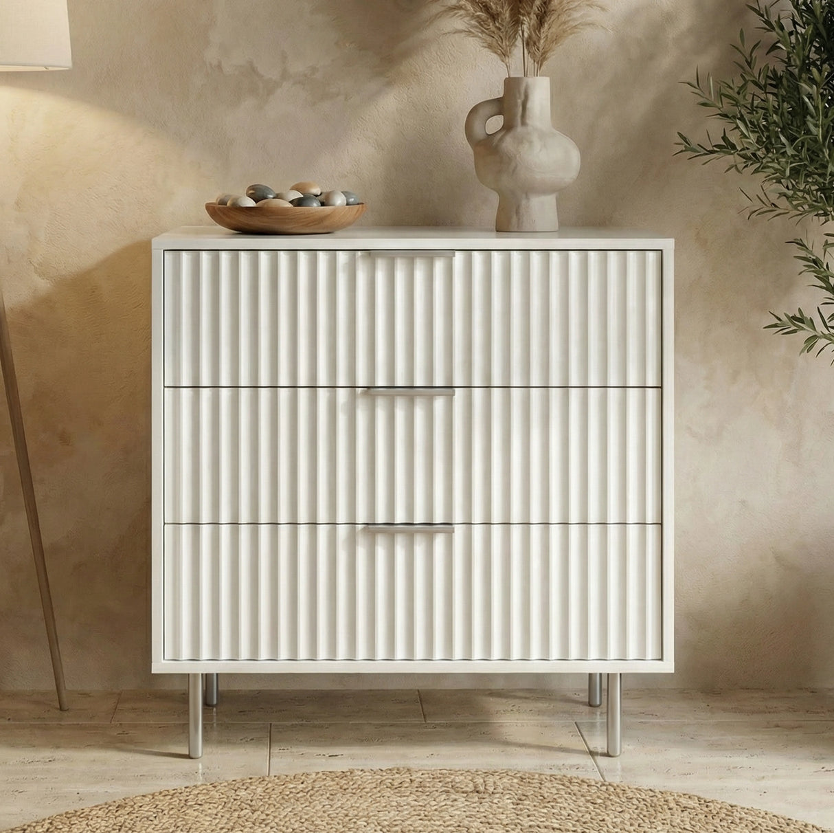 White flutrina design dresser with three drawers and silver legs placed against a wall for organised bedroom storage