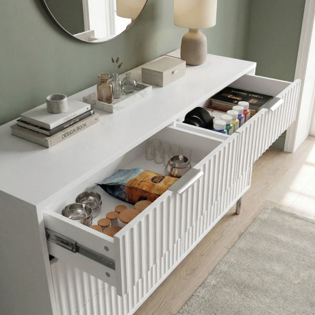 [White] chest of drawers with decorative items and open drawers against a green wall placed in a natural light room