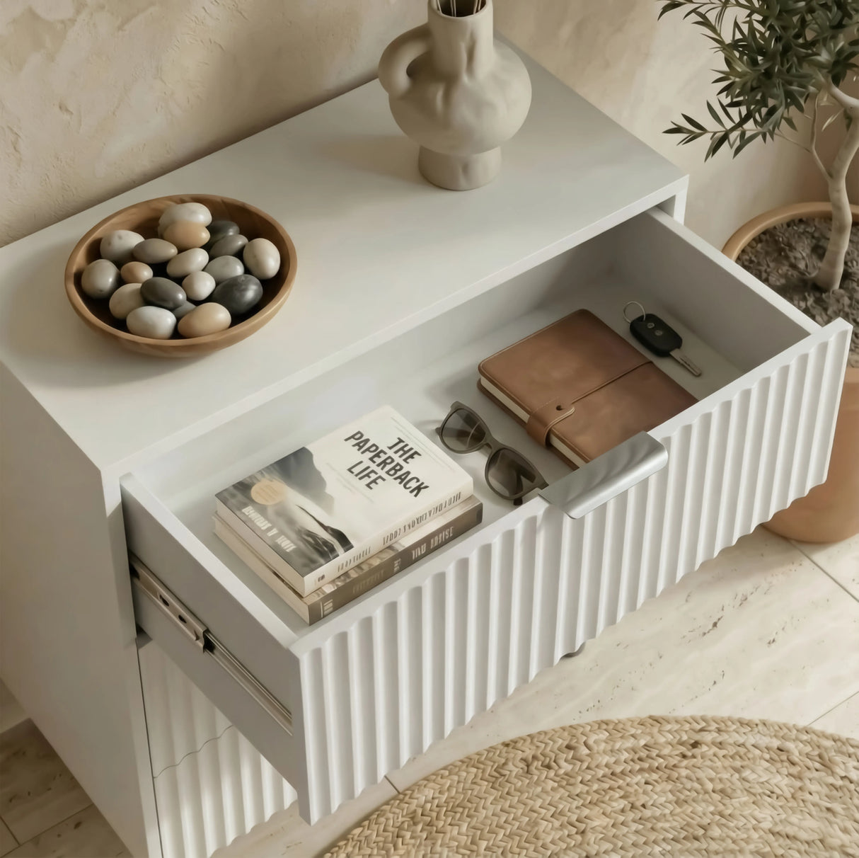 Minimalist white bedside table with an open drawer containing neatly arranged books and small items