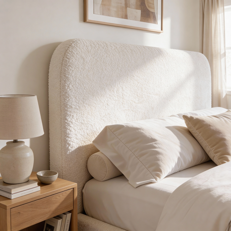Close view of white boucle king bed headboard with textured fabric upholstery and curved padded design in a modern room