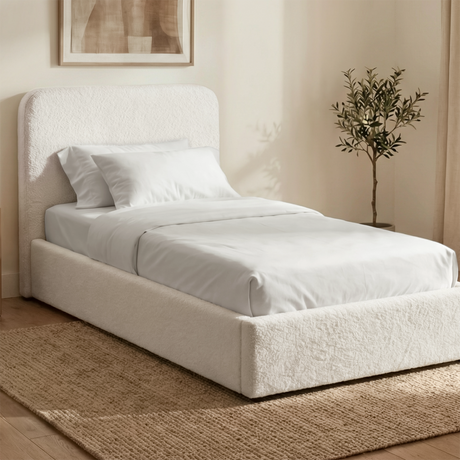 White boucle single ottoman storage bed placed in a bright interior with textured fabric upholstery and padded headboard