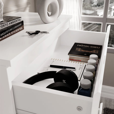 [White] close-up of open top drawer of white high gloss chest with headphones, books and accessories inside