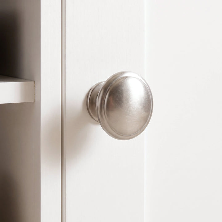 [White] round brushed metal cabinet knob mounted on a white paneled door of corner TV unit.