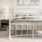 [White | King] Close view of the white curved front rail, vertical bars and taupe bedding beside a wooden table.