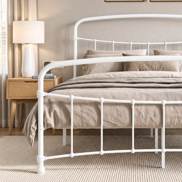 [White | King] Close view of the white curved front rail, vertical bars and taupe bedding beside a lamp.
