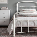 [White | Single] Close view of the white curved front rail, vertical bars and white bedding beside a small table.