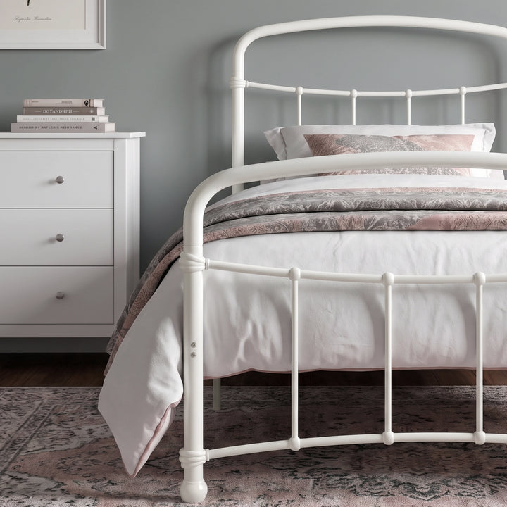 [White | Single] Close view of the white curved front rail, vertical bars and white bedding beside a small table.